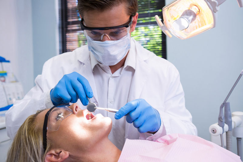 Dentist in a dental office using tools to examine a women’s mouth